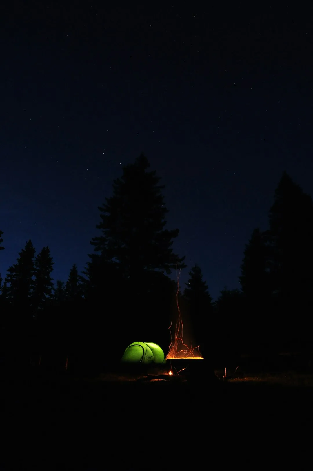 Glowing green tent beside a campfire at night under a dark sky