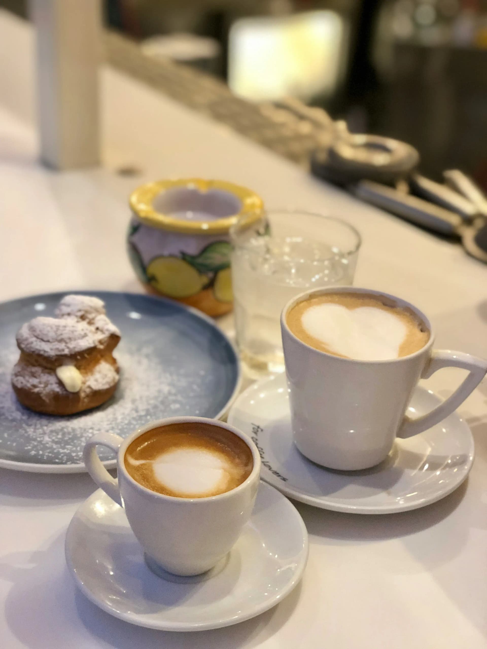Two cappuccinos and a cream puff pastry at a cafe counter