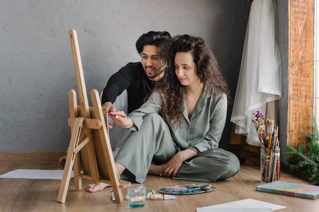 Couple sitting together painting on a canvas with brushes and paints
