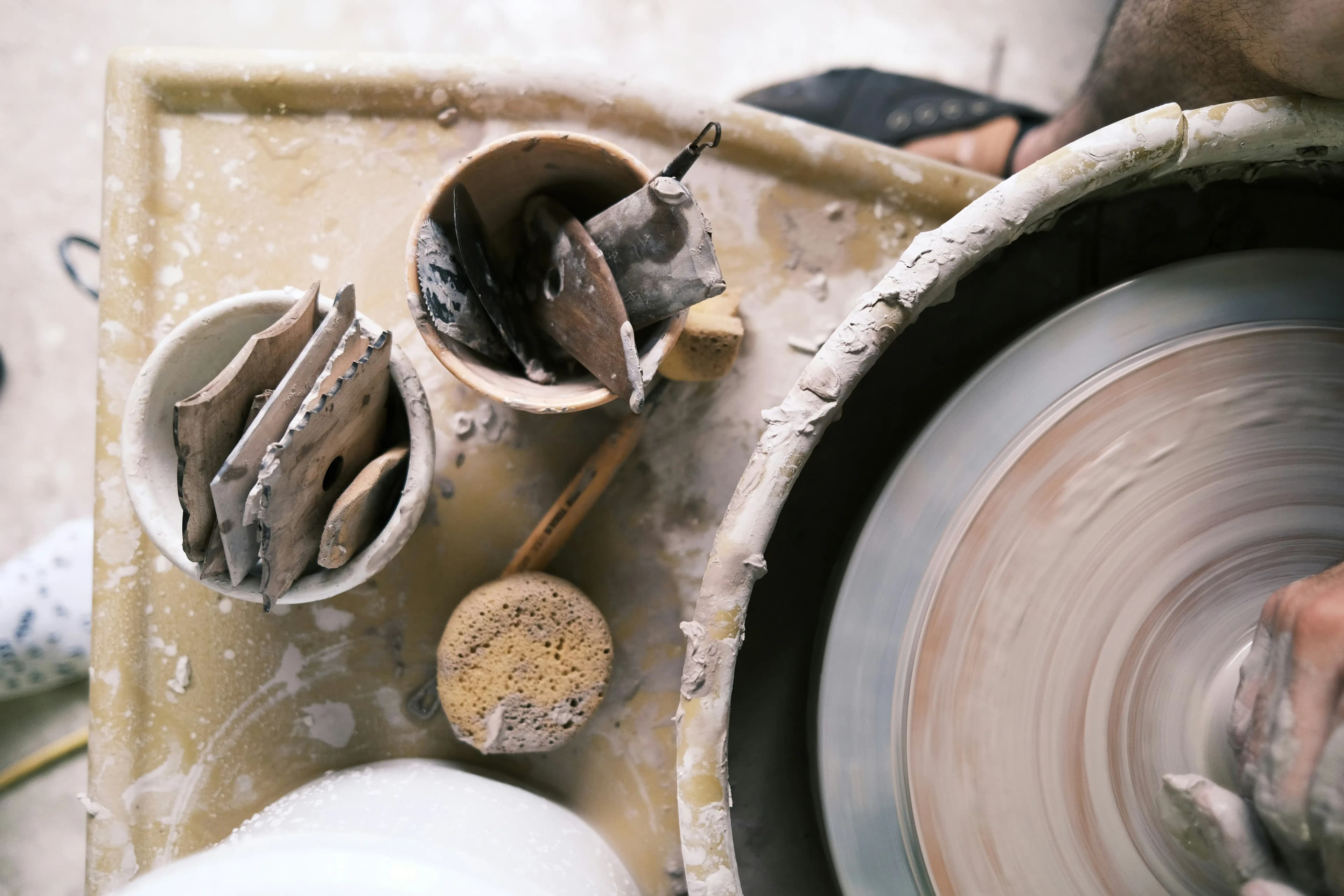 Pottery sculpting tools and supplies laid out beside a pottery wheel