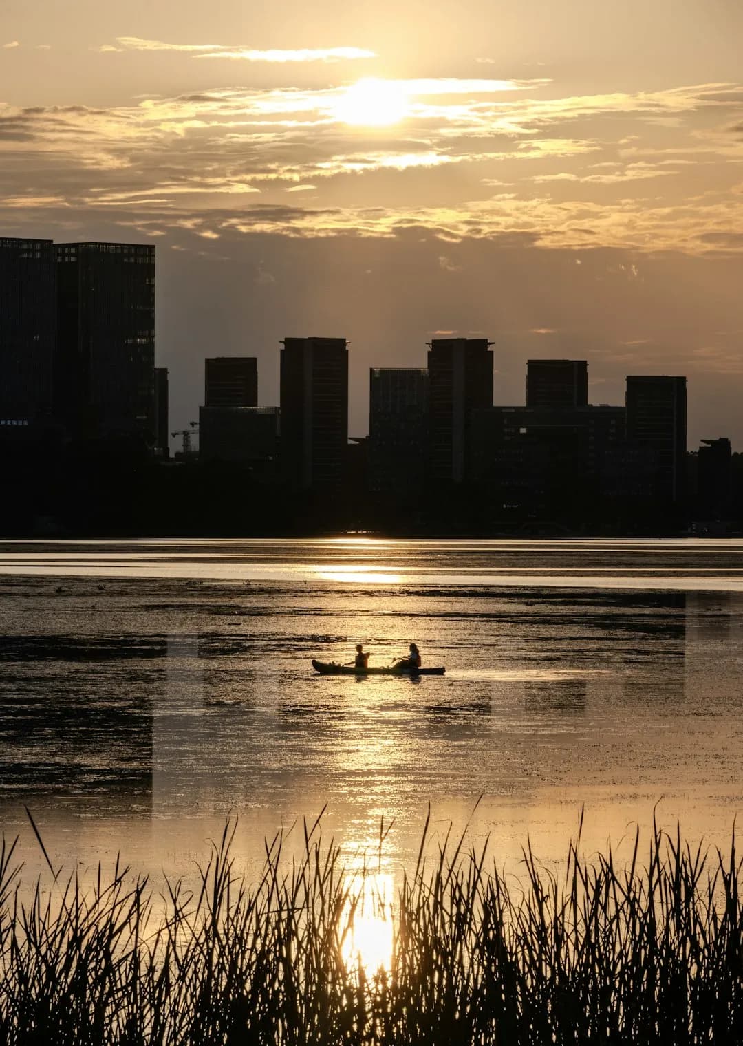 Two people in a canoe on a lake at sunset with city skyline silhouette
