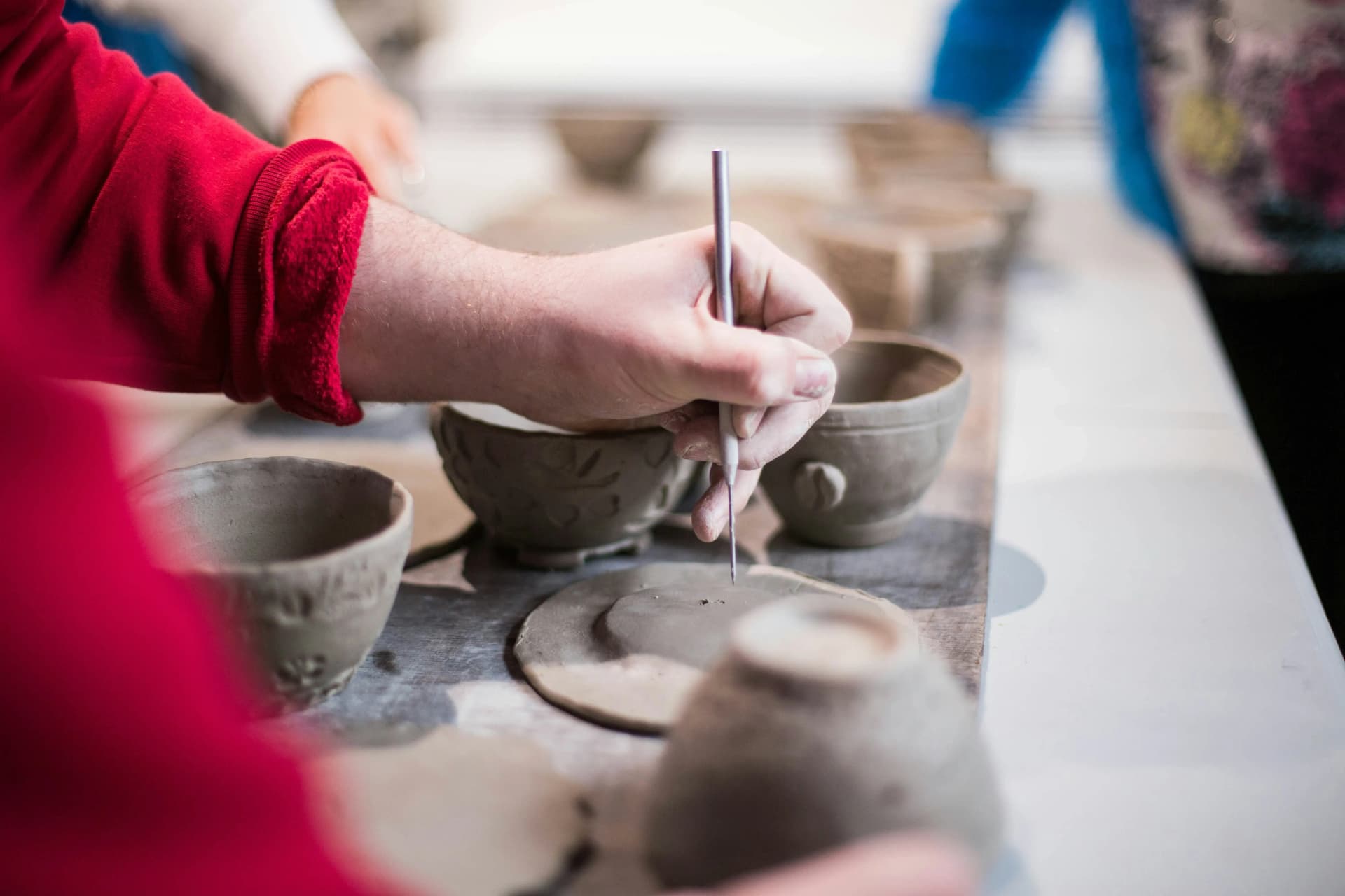 Person adding details to handmade clay bowls in a pottery class
